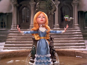 Movie still from “Santa Claus Is Comin' to Town” (1970), directed by Jules Bass – A statue of a woman in a blue dress in front of a fountain; Wide shot, Low angle