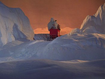 Movie still from “Santa Claus Is Comin' to Town” (1970), directed by Jules Bass – A man riding on the back of a snow covered vehicle; Extreme Wide shot, High angle