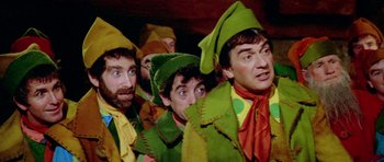 Movie still from “Santa Claus” (1985), directed by Jeannot Szwarc – A group of men dressed in green and yellow costumes; Medium shot, High angle