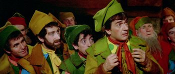 Movie still from “Santa Claus” (1985), directed by Jeannot Szwarc – A group of men dressed in green and yellow costumes; Medium shot, High angle