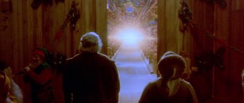Movie still from “Santa Claus” (1985), directed by Jeannot Szwarc – Two people are standing in front of an open door; Wide shot, Low angle