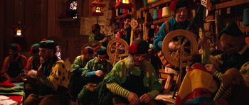 Movie still from “Santa Claus” (1985), directed by Jeannot Szwarc – A group of men in colorful hats are working in a workshop; Wide shot, High angle