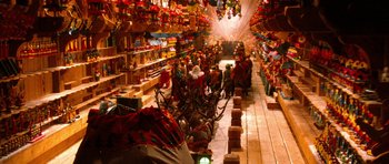 Movie still from “Santa Claus” (1985), directed by Jeannot Szwarc – A group of people sitting in a room with a lot of christmas decorations; Extreme Wide shot, High angle