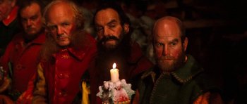 Movie still from “Santa Claus” (1985), directed by Jeannot Szwarc – A man holding a lit candle in front of another man; Close Up shot, Low angle