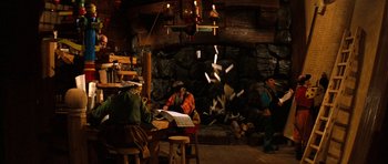 Movie still from “Santa Claus” (1985), directed by Jeannot Szwarc – A group of people sitting at a table in front of a fire place; Wide shot, High angle