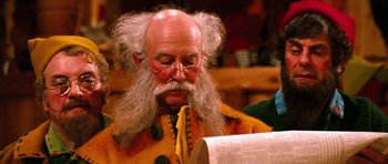 Movie still from “Santa Claus” (1985), directed by Jeannot Szwarc – An old man with long hair and a long beard is reading; Close Up shot, Over the shoulder angle