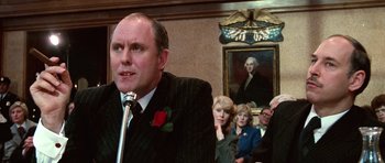 Movie still from “Santa Claus” (1985), directed by Jeannot Szwarc – A group of people sitting in front of a man with a microphone; Close Up shot, Over the shoulder angle