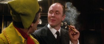 Movie still from “Santa Claus” (1985), directed by Jeannot Szwarc – A man in a pinstriped suit smoking a cigarette; Close Up shot, Over the shoulder angle