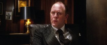 Movie still from “Santa Claus” (1985), directed by Jeannot Szwarc – A man wearing a suit and tie sitting in a chair; Close Up shot, Over the shoulder angle