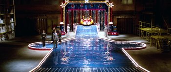 Movie still from “Santa Claus” (1985), directed by Jeannot Szwarc – Two people are standing in front of a stage; Extreme Wide shot, High angle