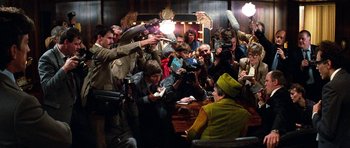 Movie still from “Santa Claus” (1985), directed by Jeannot Szwarc – A group of people taking pictures of a woman in a green dress; Wide shot, Over the shoulder angle