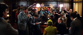 Movie still from “Santa Claus” (1985), directed by Jeannot Szwarc – A group of people standing around a bar with cameras; Wide shot, Over the shoulder angle