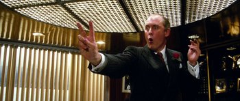 Movie still from “Santa Claus” (1985), directed by Jeannot Szwarc – A man in a suit and tie holding his hand up in the air; Close Up shot, Low angle