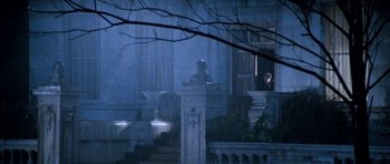Movie still from “Santa Claus” (1985), directed by Jeannot Szwarc – A statue of a person sitting on a pedestal in front of a building; Wide shot, Over the shoulder angle