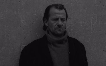 Movie still from “Satantango” (1994), directed by Béla Tarr – A black and white photo of a man in a sweater; Close Up shot, Low angle