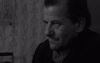 Movie still from “Satantango” (1994), directed by Béla Tarr – Black and white photograph of a man looking at the camera; Close Up shot, Over the shoulder angle