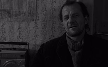 Movie still from “Satantango” (1994), directed by Béla Tarr – A black and white photo of a man in a jacket and tie; Close Up shot, Over the shoulder angle