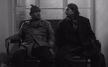Movie still from “Satantango” (1994), directed by Béla Tarr – Two men are sitting on a bench and talking; Medium shot, Low angle