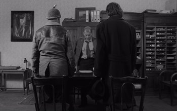 Movie still from “Satantango” (1994), directed by Béla Tarr – A group of people sitting around a table; Medium shot, Over the shoulder angle