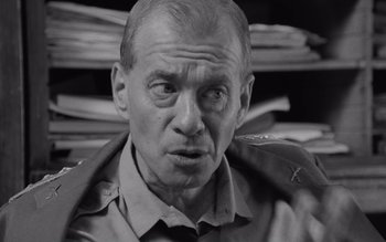 Movie still from “Satantango” (1994), directed by Béla Tarr – An older man in a military uniform stares at the camera; Close Up shot, Over the shoulder angle
