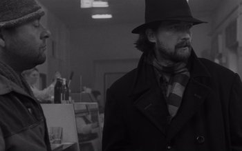 Movie still from “Satantango” (1994), directed by Béla Tarr – A black and white photo of a man wearing a hat; Medium shot, Low angle