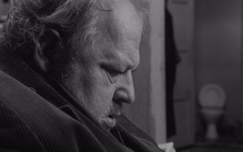Movie still from “Satantango” (1994), directed by Béla Tarr – An older man is looking down at his face; Close Up shot, High angle