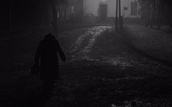 Movie still from “Satantango” (1994), directed by Béla Tarr – A person walking on a path in the dark; Wide shot, High angle