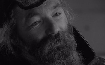 Movie still from “Satantango” (1994), directed by Béla Tarr – Black and white photograph of a man with long beard; Extreme Close Up shot, Over the shoulder angle