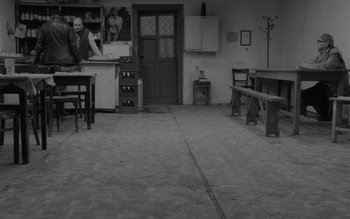 Movie still from “Satantango” (1994), directed by Béla Tarr – An empty room with a table and chairs and an open door; Wide shot, High angle