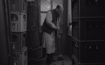 Movie still from “Satantango” (1994), directed by Béla Tarr – An old man sweeping the floor in a room; Wide shot, High angle