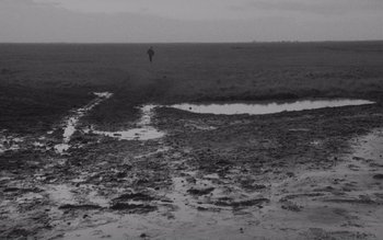 Movie still from “Satantango” (1994), directed by Béla Tarr – A person flying a kite on a beach; Extreme Wide shot, High angle
