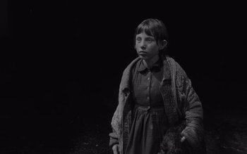 Movie still from “Satantango” (1994), directed by Béla Tarr – A young girl wearing a dress and holding a teddy bear; Medium shot, High angle