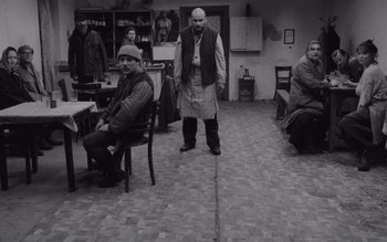 Movie still from “Satantango” (1994), directed by Béla Tarr – A group of people sitting in a room; Wide shot, High angle