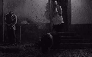 Movie still from “Satantango” (1994), directed by Béla Tarr – A man standing in front of an entrance to a building; Wide shot, Low angle