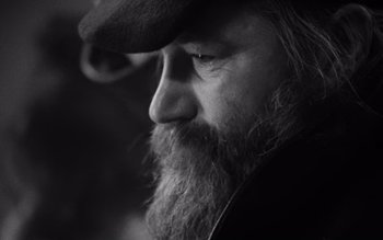 Movie still from “Satantango” (1994), directed by Béla Tarr – A man with a long beard wearing a hat; Extreme Close Up shot, Low angle
