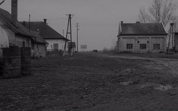 Movie still from “Satantango” (1994), directed by Béla Tarr – An empty field with a few houses in the background; Extreme Wide shot, Low angle