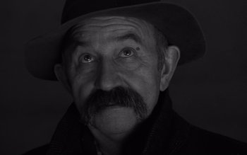 Movie still from “Satantango” (1994), directed by Béla Tarr – An old man with a mustache wearing a hat; Close Up shot, Low angle