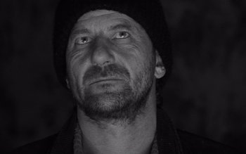 Movie still from “Satantango” (1994), directed by Béla Tarr – Black and white photograph of a man wearing a hat; Close Up shot, Low angle