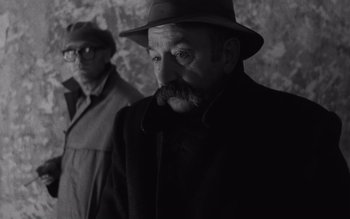 Movie still from “Satantango” (1994), directed by Béla Tarr – A man in a hat and a man in a coat; Close Up shot, Over the shoulder angle
