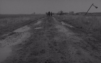 Movie still from “Satantango” (1994), directed by Béla Tarr – Three people are walking down a dirt road; Extreme Wide shot, High angle