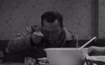Movie still from “Satantango” (1994), directed by Béla Tarr – A black and white photo of a man eating food; Close Up shot, High angle