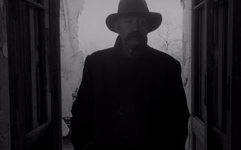 Movie still from “Satantango” (1994), directed by Béla Tarr – A black and white photo of a man wearing a hat; Medium shot, Low angle