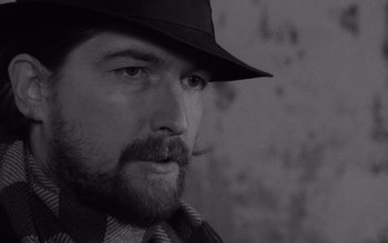 Movie still from “Satantango” (1994), directed by Béla Tarr – A man wearing a hat and a tie; Close Up shot, Over the shoulder angle