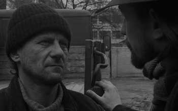 Movie still from “Satantango” (1994), directed by Béla Tarr – A black - and - white photo of a man looking at another man; Close Up shot, Over the shoulder angle