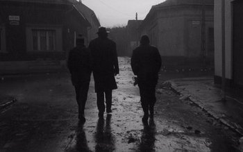 Movie still from “Satantango” (1994), directed by Béla Tarr – Three men are walking down the street in the rain; Wide shot, Low angle