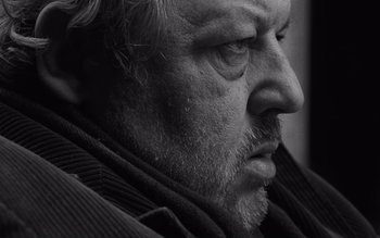 Movie still from “Satantango” (1994), directed by Béla Tarr – Black and white photograph of an older man's face; Close Up shot, Low angle