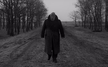 Movie still from “Satantango” (1994), directed by Béla Tarr – An old man walking down a dirt road; Wide shot, Low angle