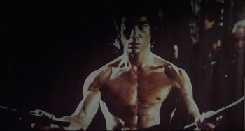 Movie still from “Saturday Night Fever” (1977), directed by John Badham – A man with no shirt is posing for a picture; Medium shot, Low angle