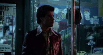 Movie still from “Saturday Night Fever” (1977), directed by John Badham – A man in a red leather jacket smoking a cigarette; Medium shot, Over the shoulder angle