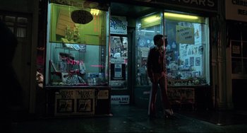Movie still from “Saturday Night Fever” (1977), directed by John Badham – A person standing in front of a store at night; Wide shot, Low angle